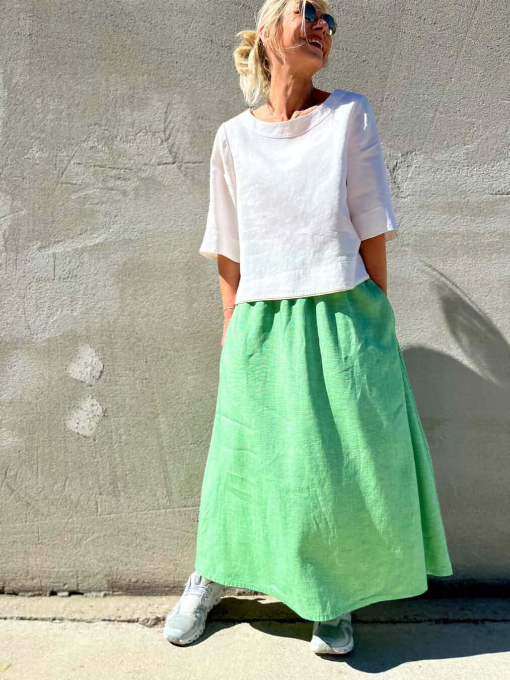 A woman wearing a white silk blouse and a green Claude skirt against a gray wall.