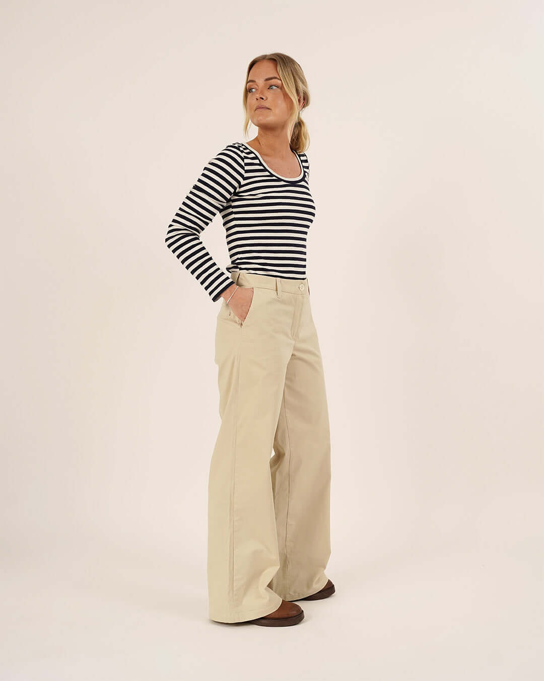 Woman wearing a striped shirt and beige pants on a white background