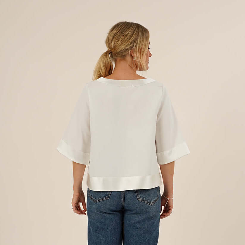 Woman wearing the Silke Blouse sewing pattern in white silk and a pair of Jeans, seen from the back