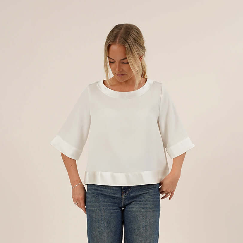 A woman wearing a white Silke Blouse sewing pattern, and blue jeans against a plain background