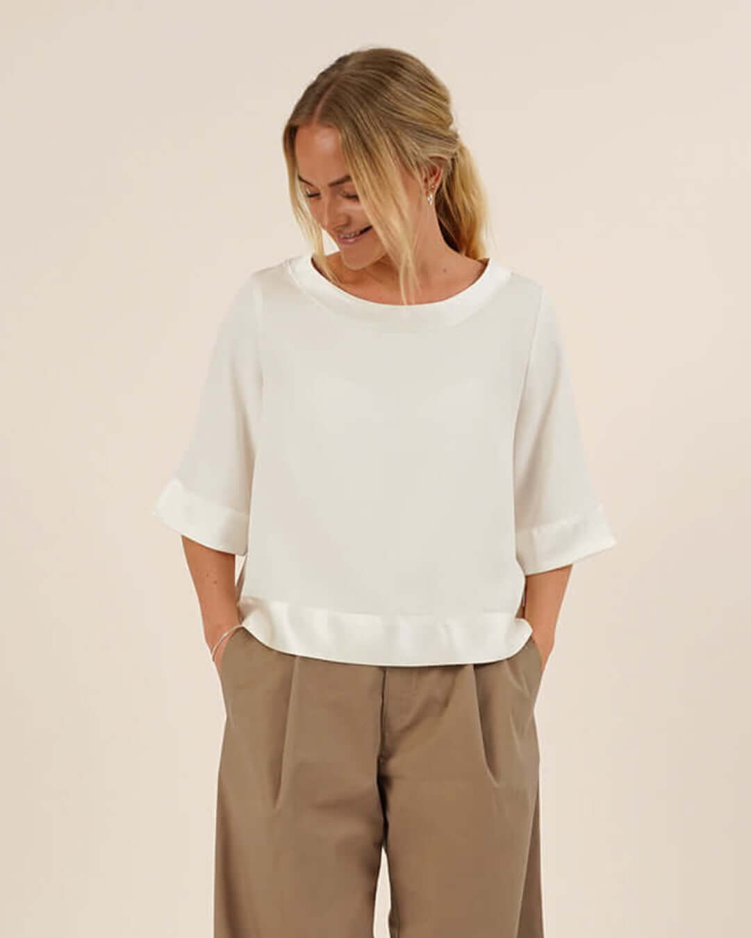 Woman wearing the Silke Blouse sewing pattern in white silk and a pair of beige Bermuda Pants