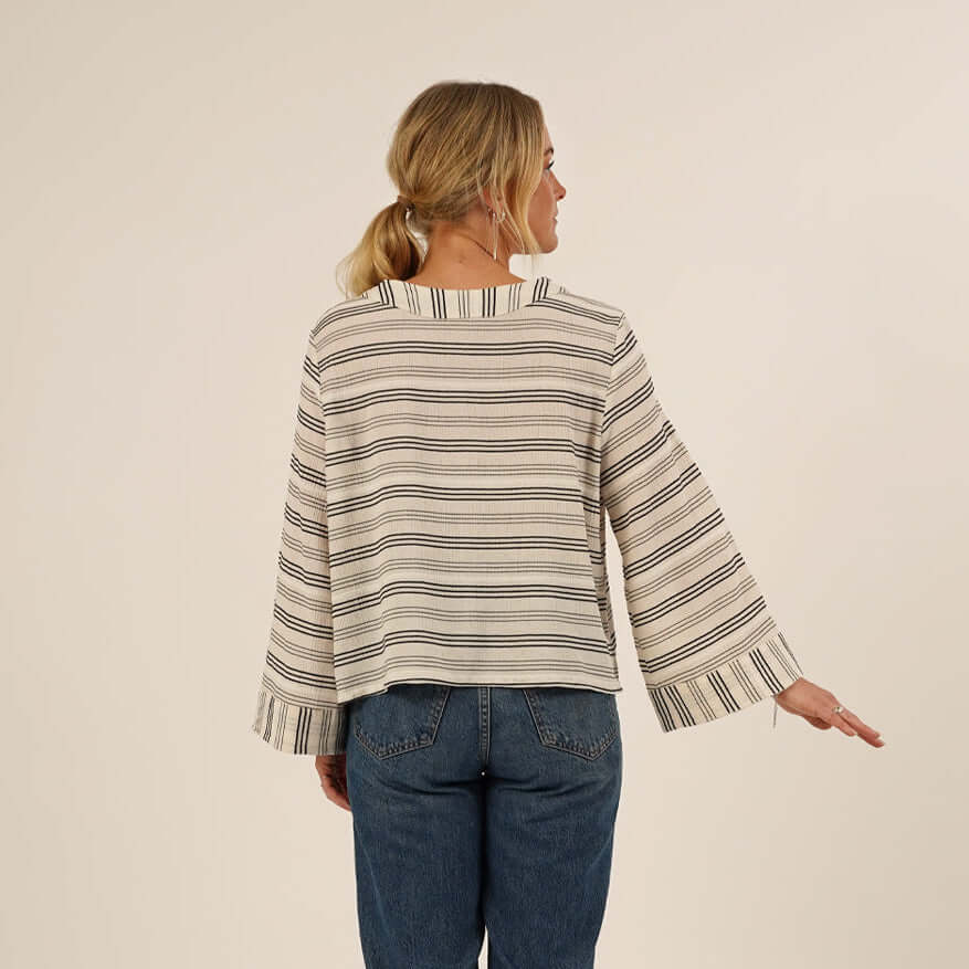Woman wearing the Silke Blouse sewing pattern seen from the back, and a pair of Jeans