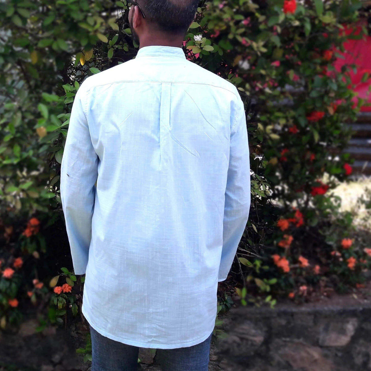 Back view of a Men's Tunic paper pattern with a banded collar and relaxed fit, surrounded by flowers.