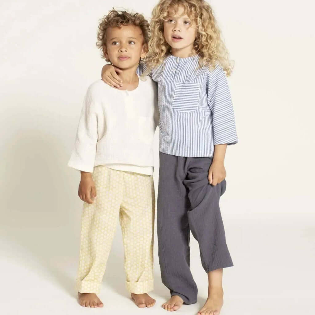 Two children wearing the Una shirt sewing pattern, showcasing a striped top with a pocket and casual pants, size 3-12 years.
