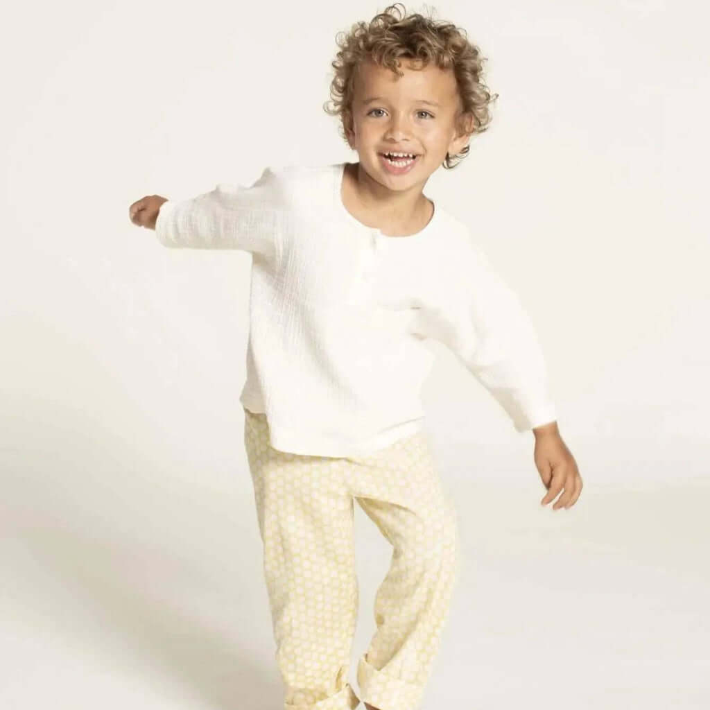Una shirt sewing pattern size 3-12 years modeled by a smiling child in a white top and yellow polka dot pants.