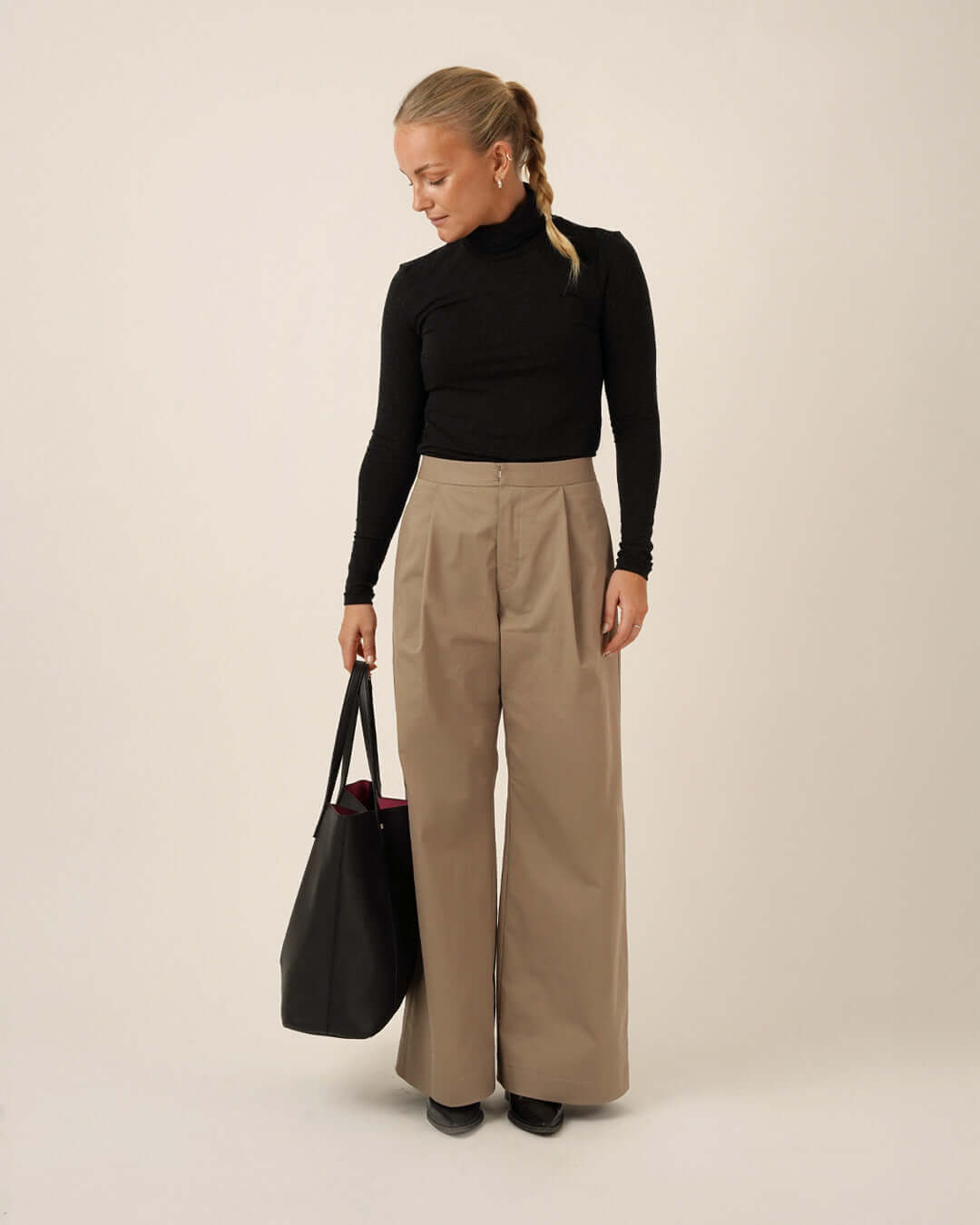 Model wearing high-waisted Bermuda Pants and Shorts Sewing Pattern with a black top and holding a black tote bag.