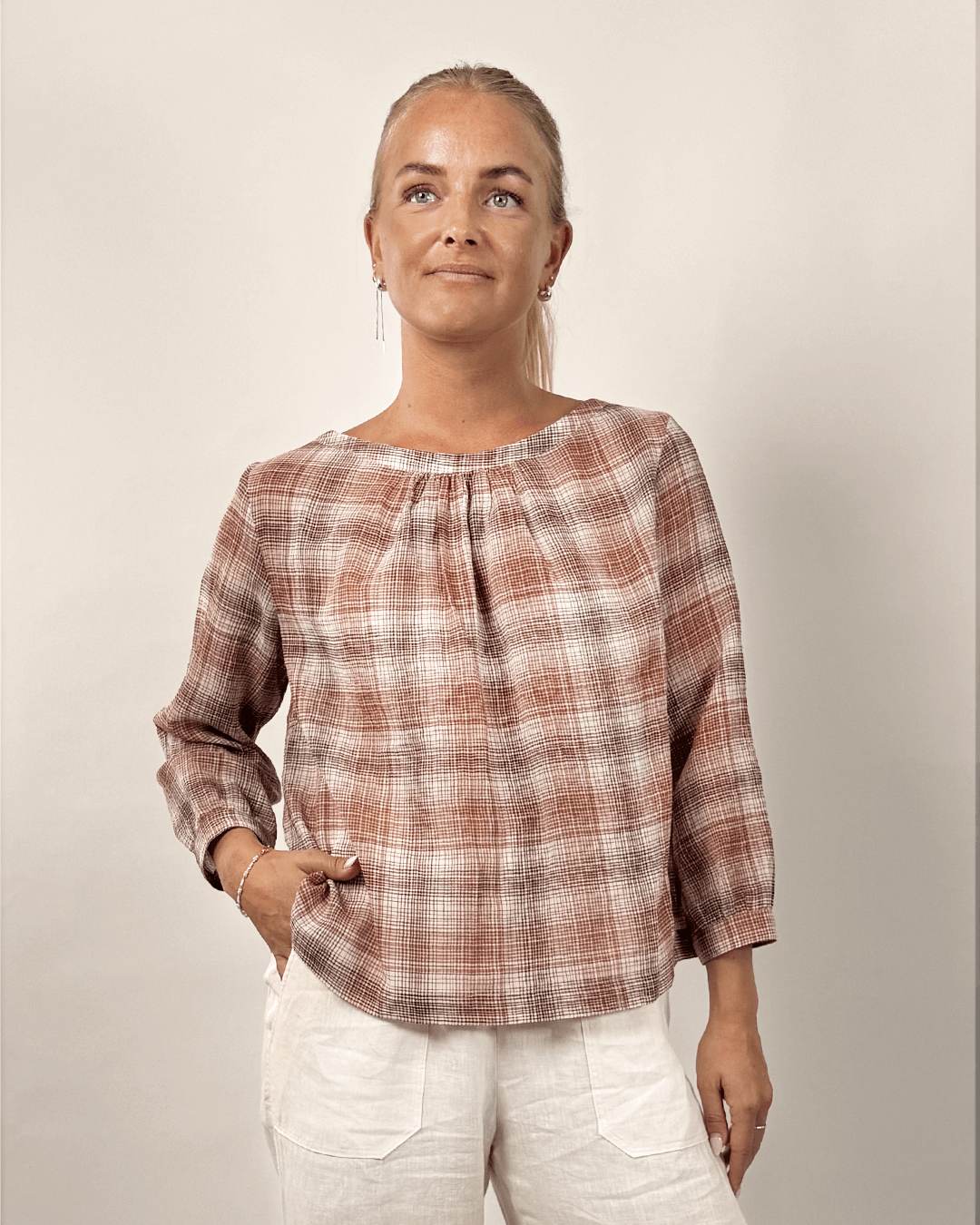 Esther Blouse Paper Pattern modeled in a stylish plaid fabric featuring pleats at the neckline and gathered sleeves.