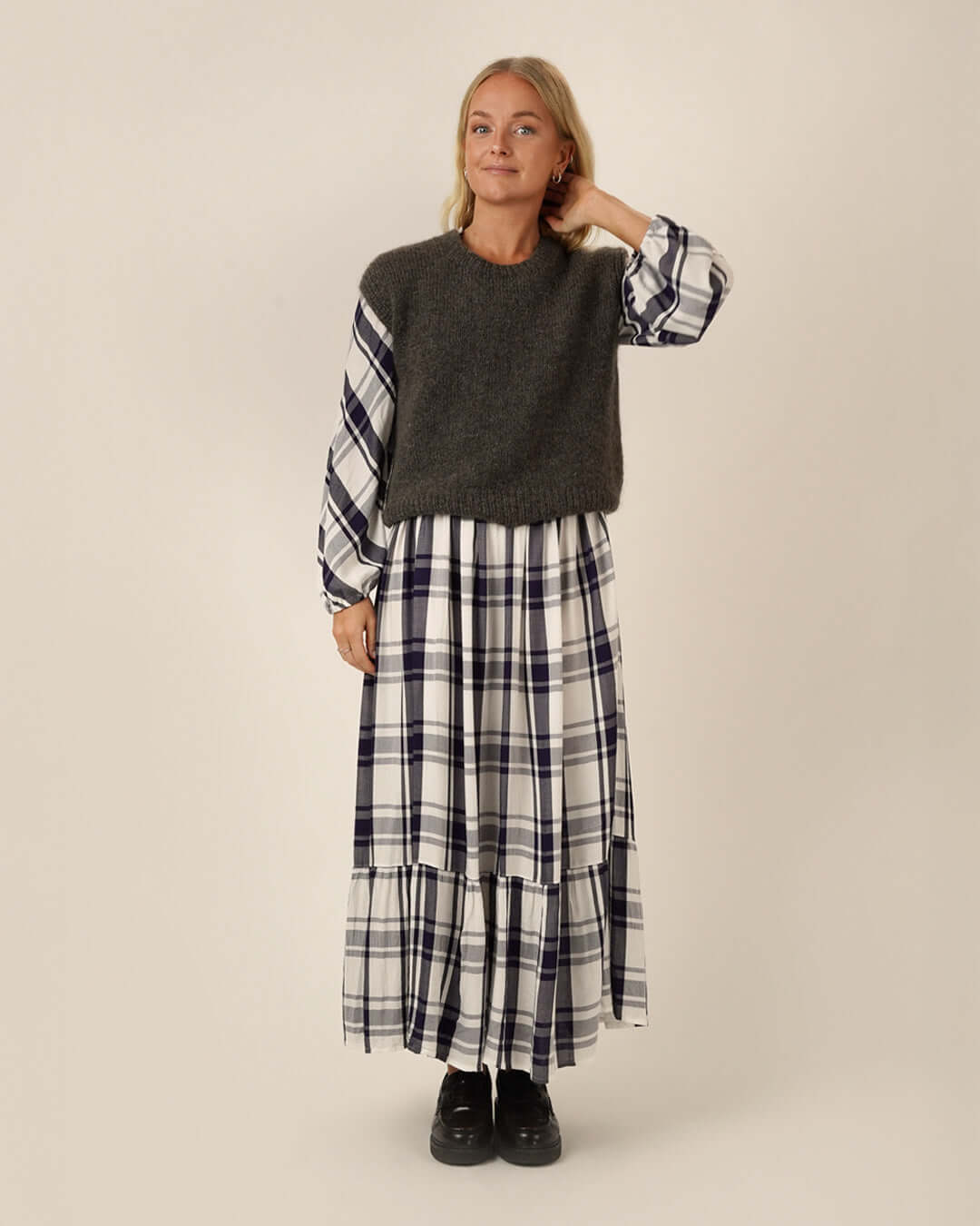 Woman wearing a dark gray sweater and plaid Freedom dress sewing pattern on a plain background