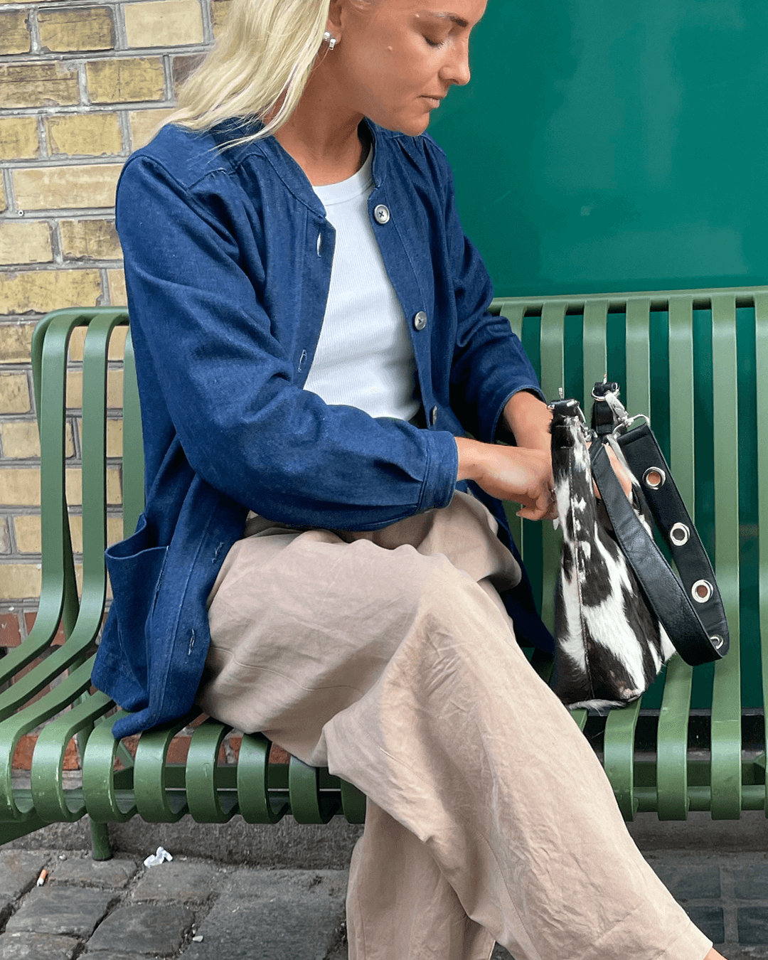Woman wearing the Artist Jacket Paper Pattern in denim color, sitting on a bench, styled with wide-leg trousers and a handbag.