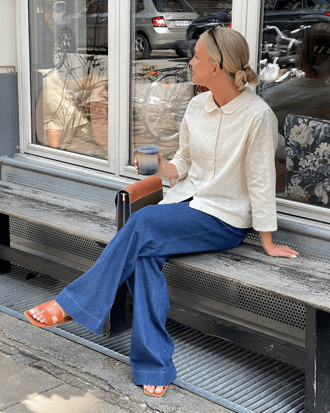 Woman wearing Dukke Blouse Paper Pattern with relaxed fit and Peter Pan collar, seated outdoors.