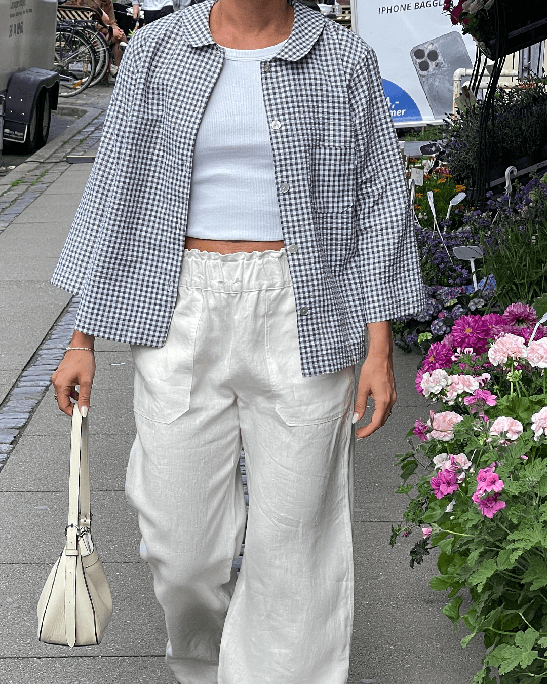Woman wearing a relaxed-fit Dukke Blouse Paper Pattern in checkered fabric, styled with wide white trousers.