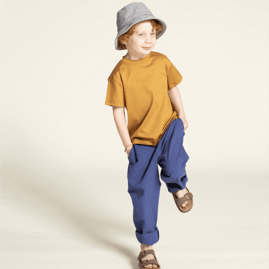 Child wearing Kids' Volume Pants pattern with a yellow shirt and a blue bucket hat, showcasing a playful outfit.