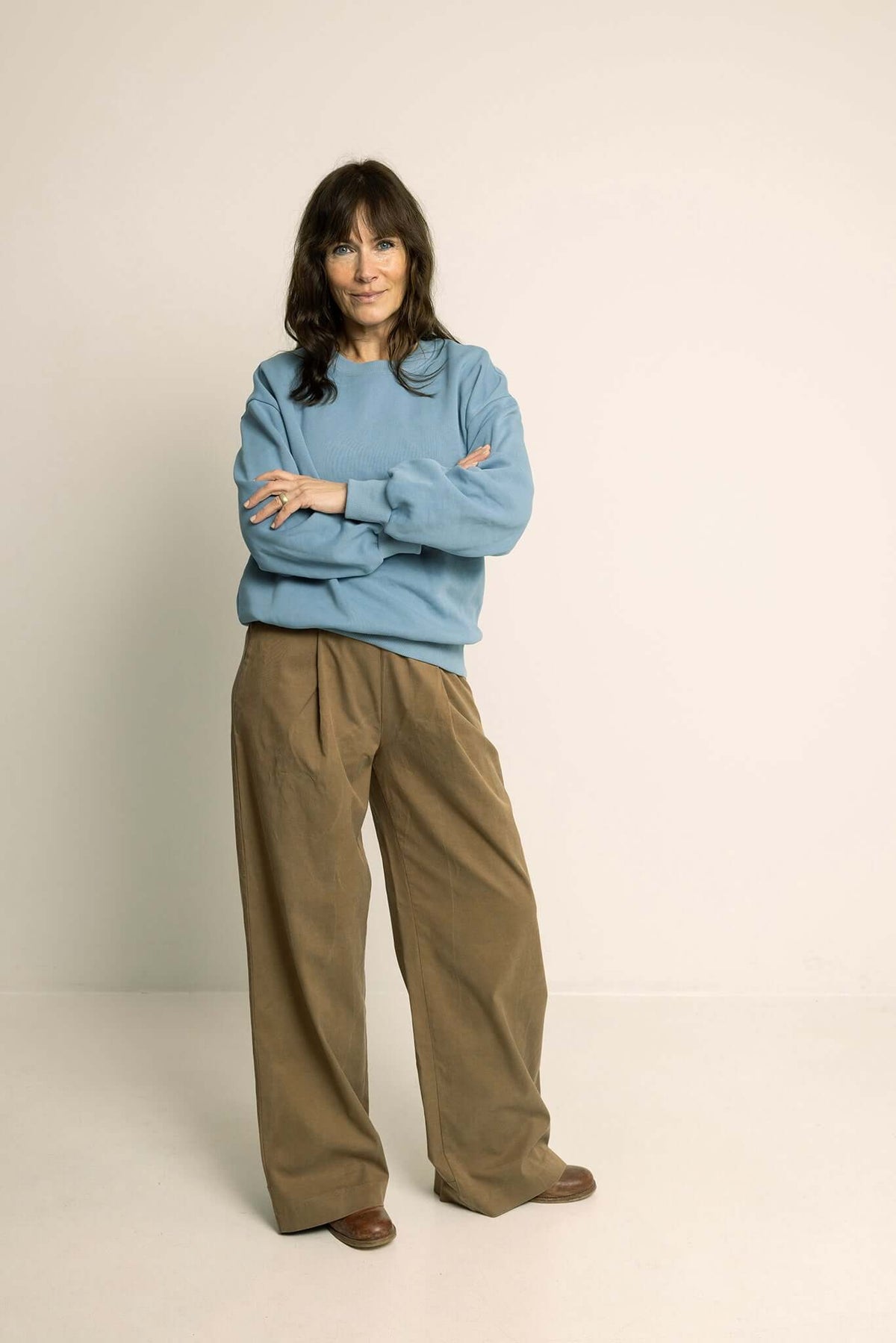 Woman in a blue sweater and brown Palazzo Pants Paper Pattern standing confidently with arms crossed.