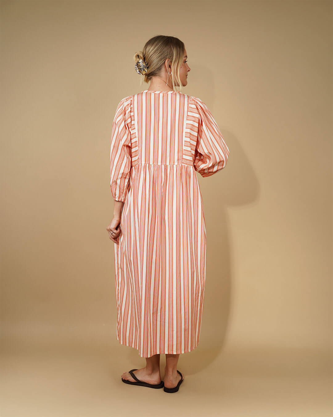 Woman wearing a long, Balka Dress sewing pattern striped dress against a beige background