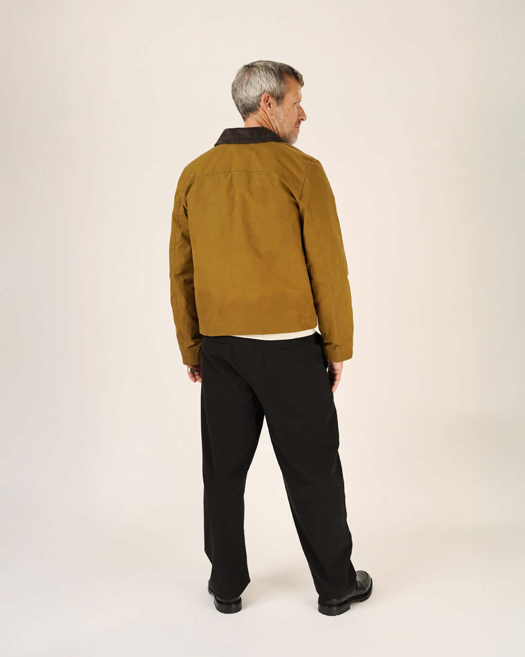 Man wearing a brown jacket and Volume Pants Sewing Pattern, showcasing the back view and comfortable fit.