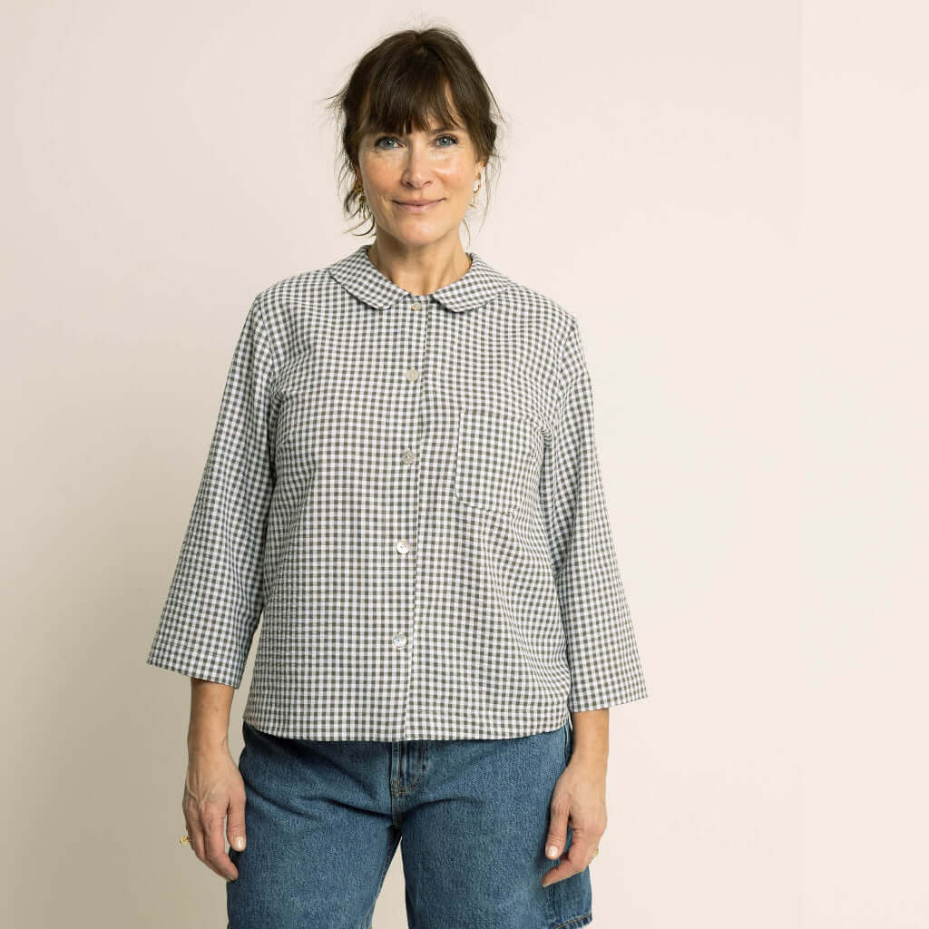 Dukke Blouse Paper Pattern worn by a smiling woman featuring a flat collar and button-up design in a checked pattern.