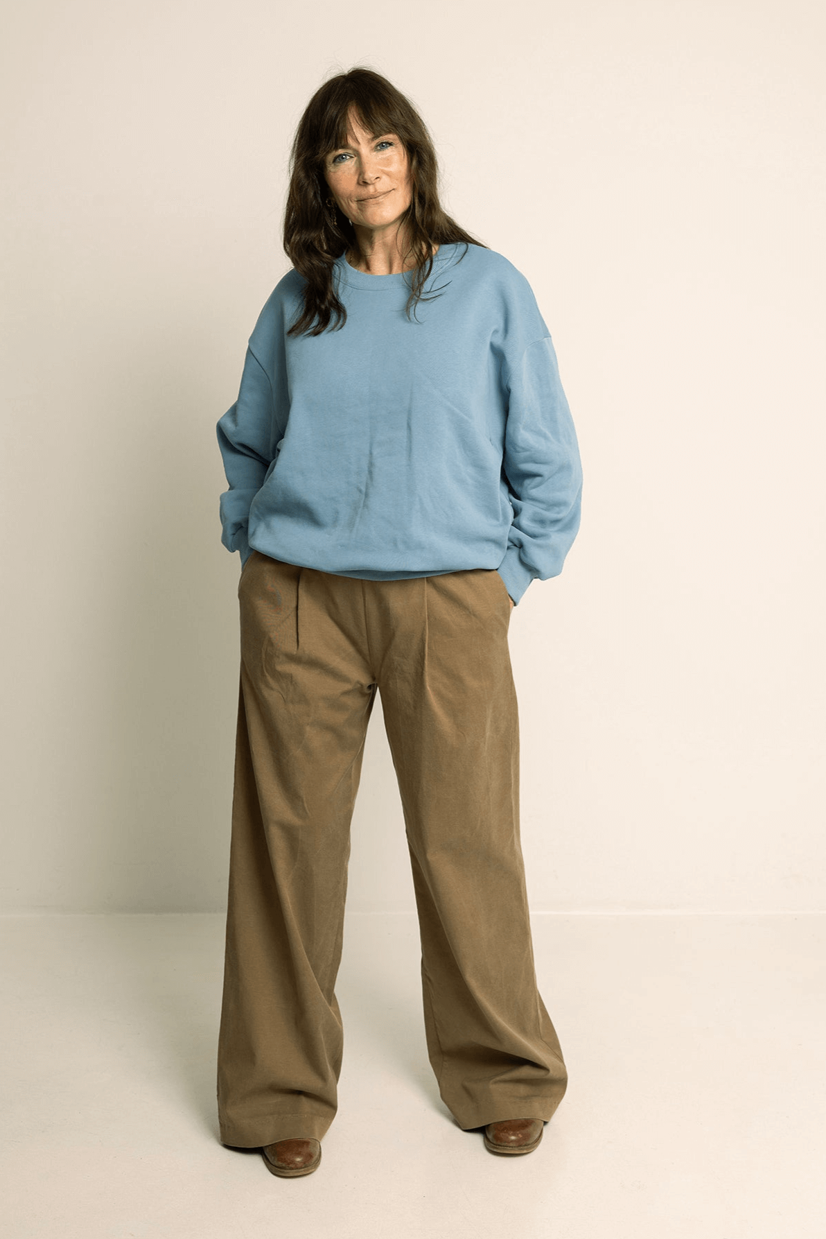 Woman wearing a blue sweatshirt and brown Palazzo Pants Paper Pattern, showcasing wide-leg design.