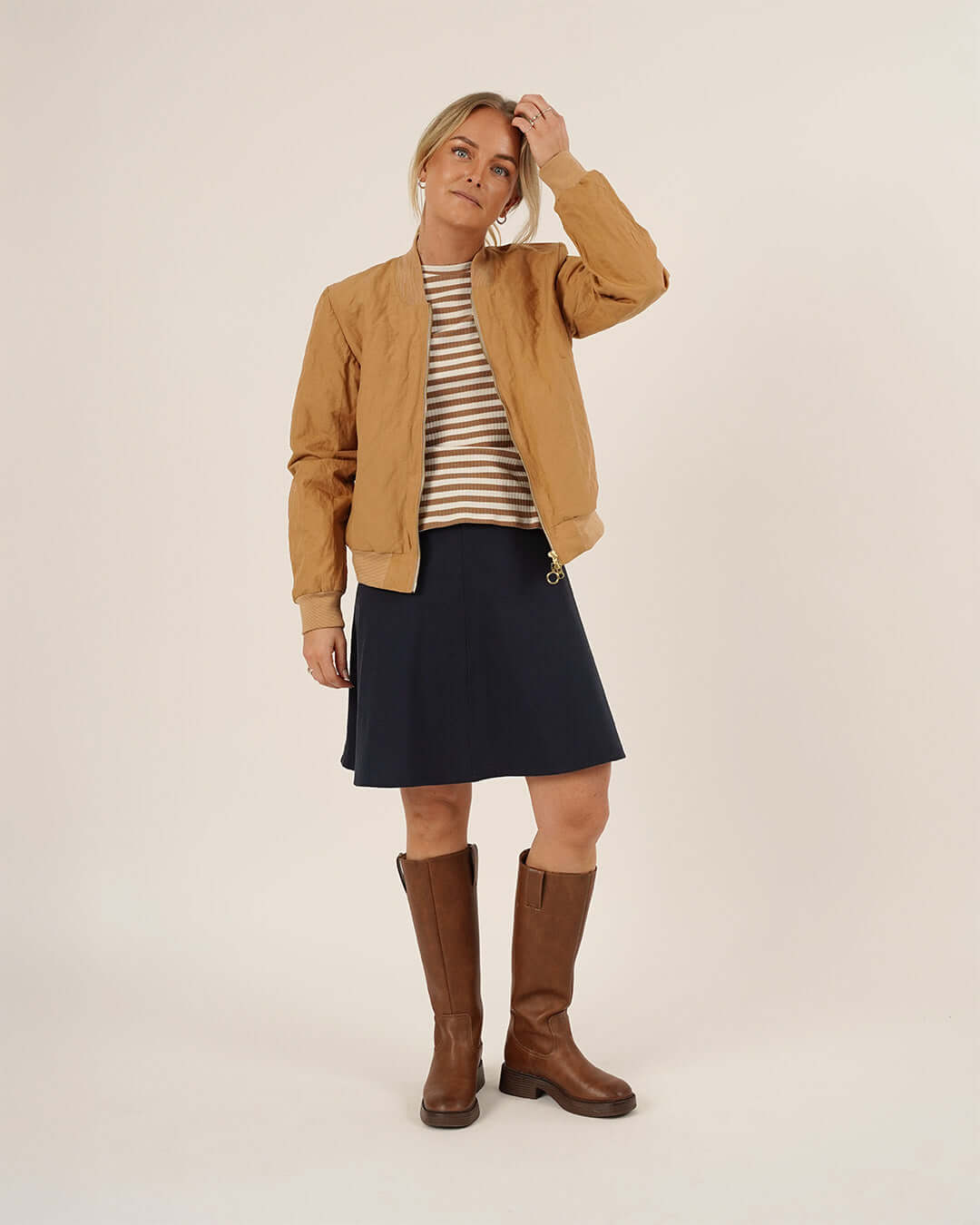 Woman wearing the Amelia Bomber Jacket sewing pattern in camel fabric layered over a striped knit top and paired with the Linea Skirt sewing pattern in navy fabric