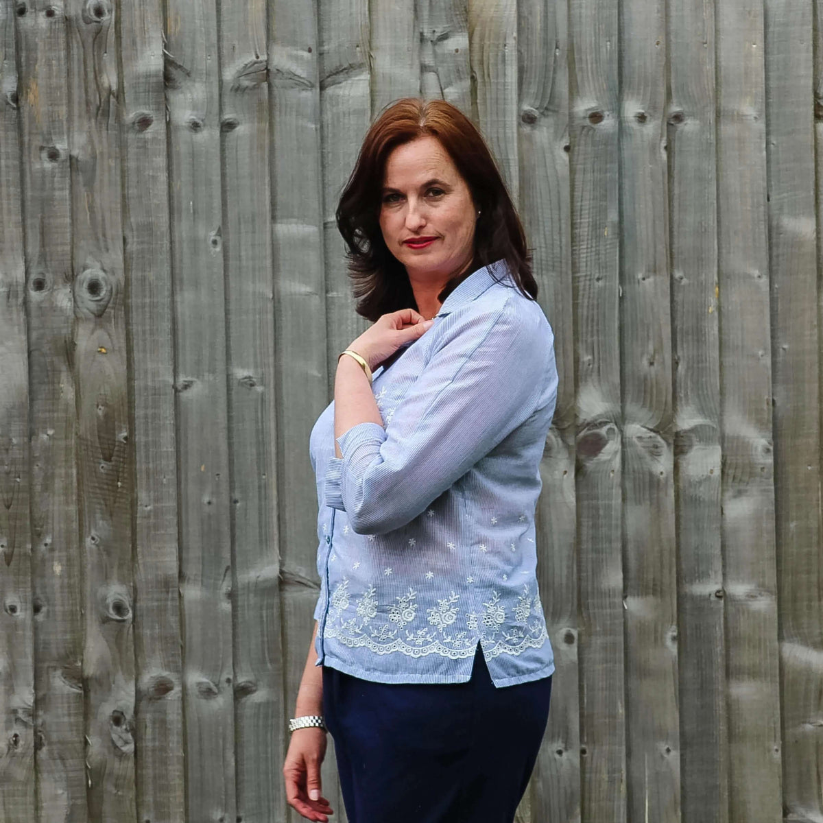 Woman wearing a light blue Tropicana shirt Paper Pattern with a relaxed fit and 3/4-length sleeves against a wooden backdrop.