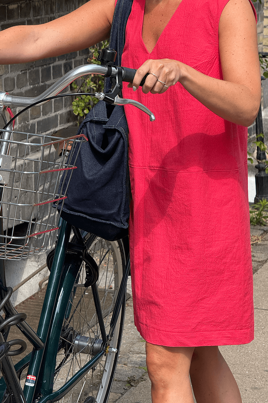 A woman in a bright pink dress holds a bicycle, showcasing the City Dress Sewing Pattern in a casual setting.