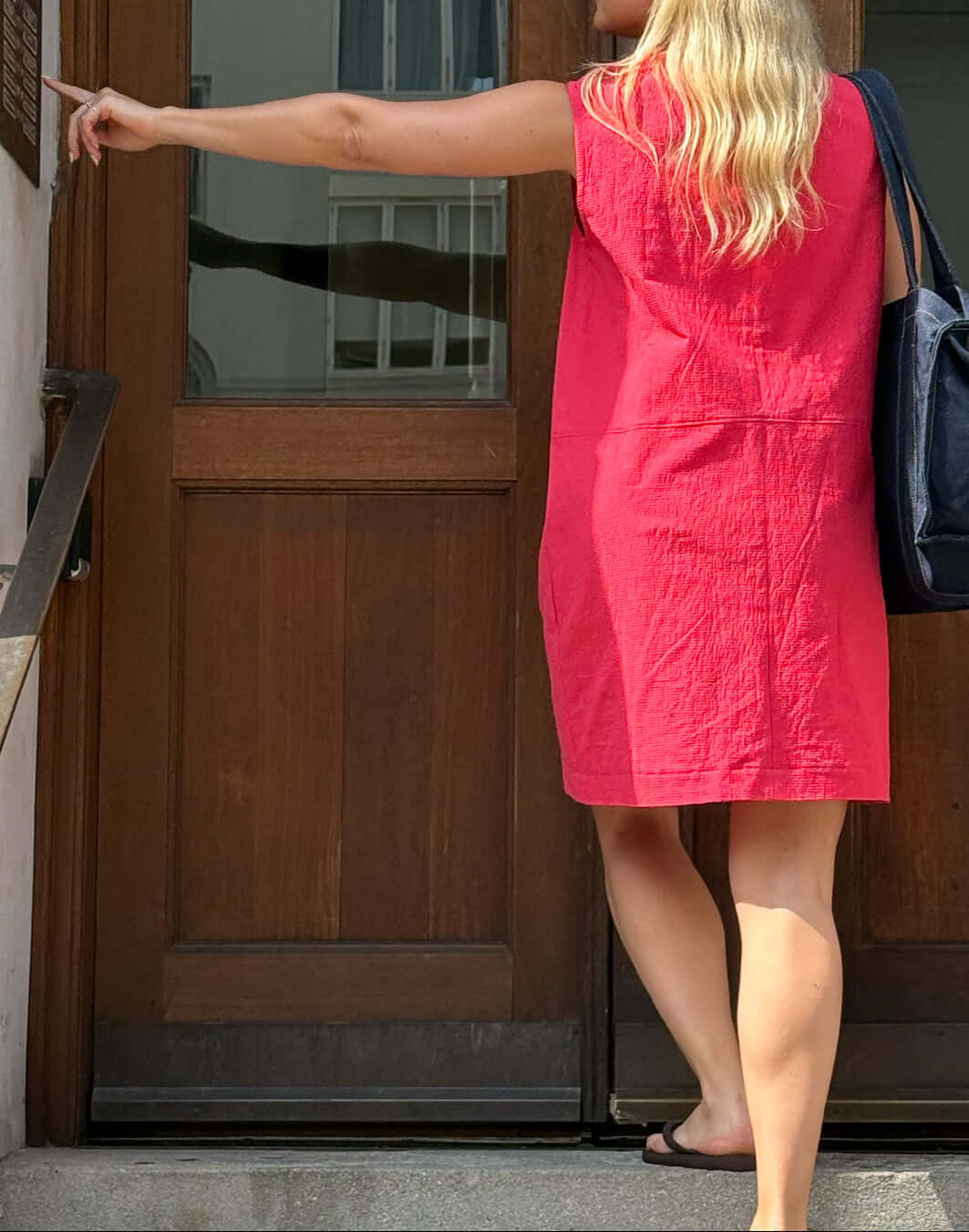 Woman wearing a sleeveless City Dress Sewing Pattern, standing outside a wooden door.
