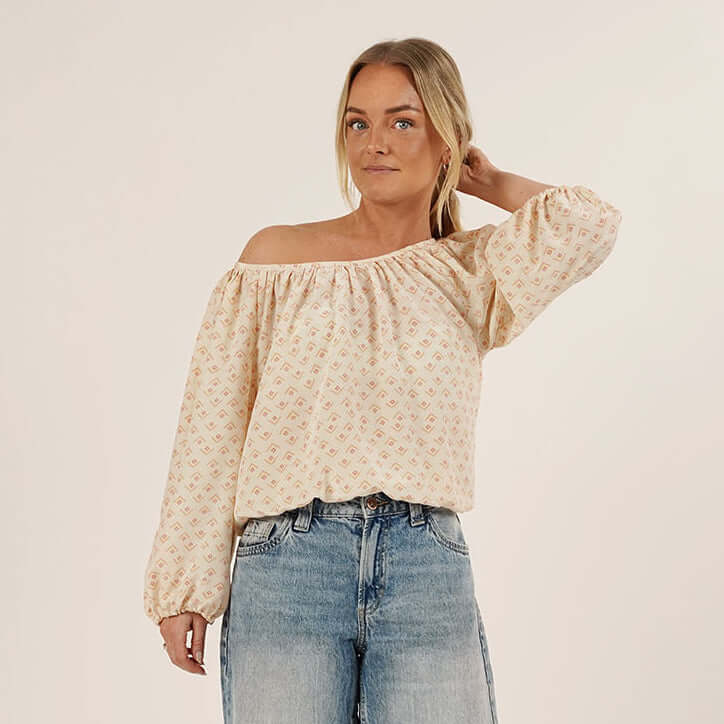 Woman wearing a beige off-shoulder top and denim shorts on a plain background