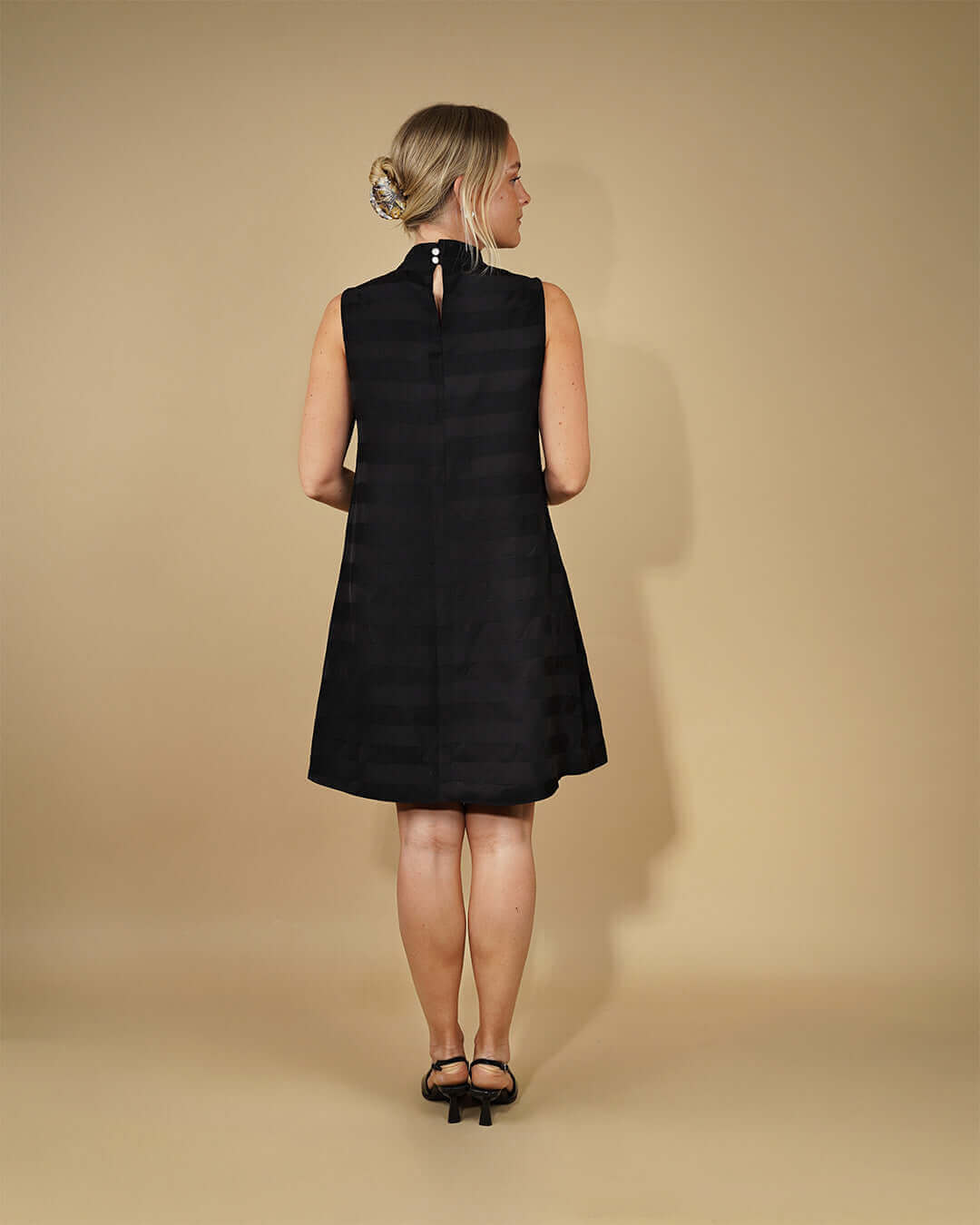 Back view of a model wearing the June Dress Sewing Pattern in black with a halterneck collar and button closure.