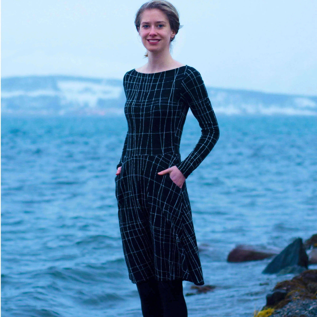 Model wearing Asta dress Paper Pattern by the water, showcasing the fitted bodice and semi-circular A-line skirt.