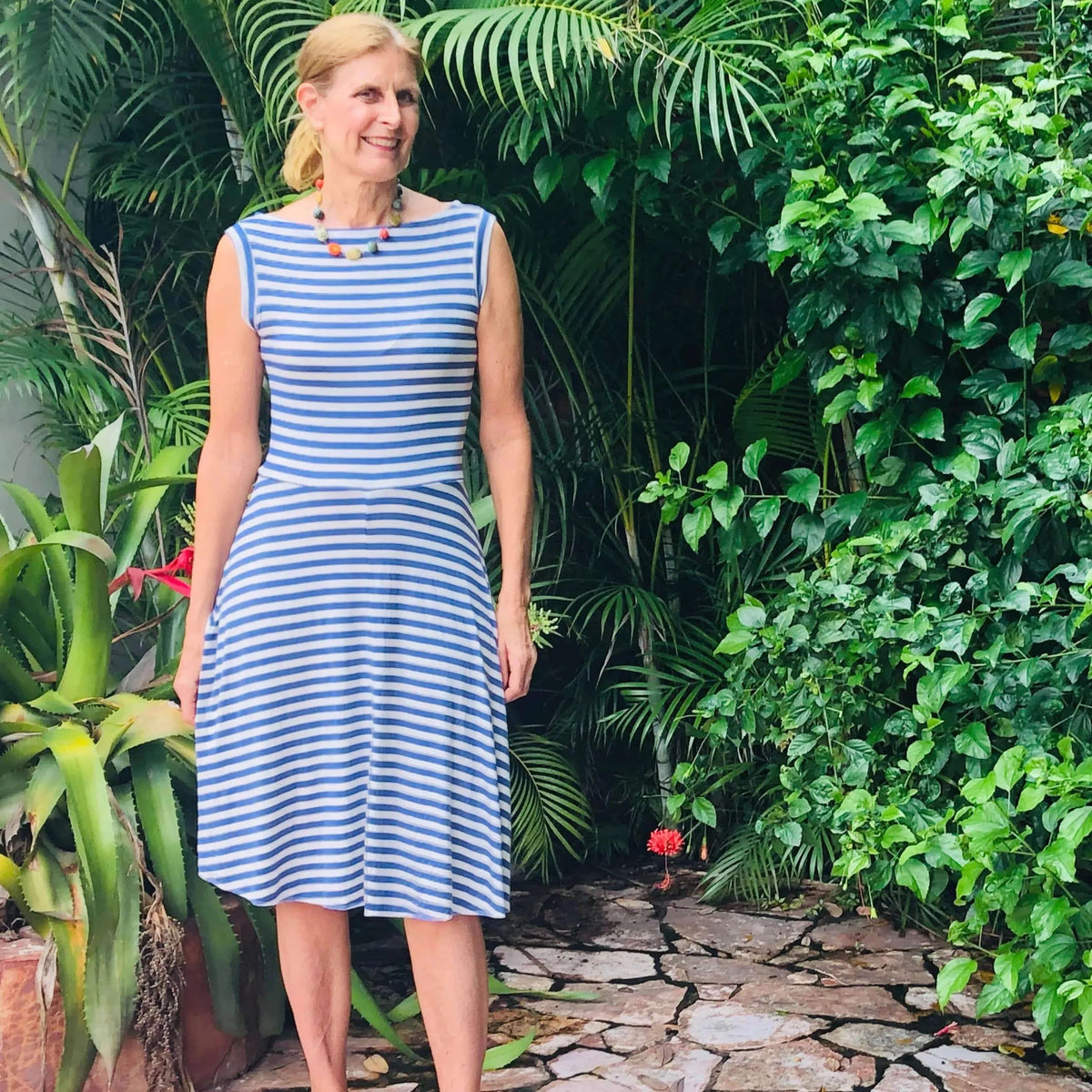 Woman wearing Asta dress Paper Pattern with stripes, standing amidst lush greenery, showcasing a flattering A-line silhouette.