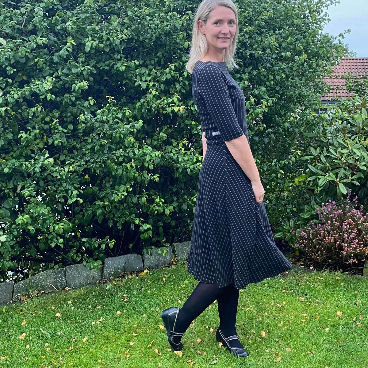 Asta dress Paper Pattern modeled by a woman in a garden, showcasing its fitted bodice and flowing A-line skirt.