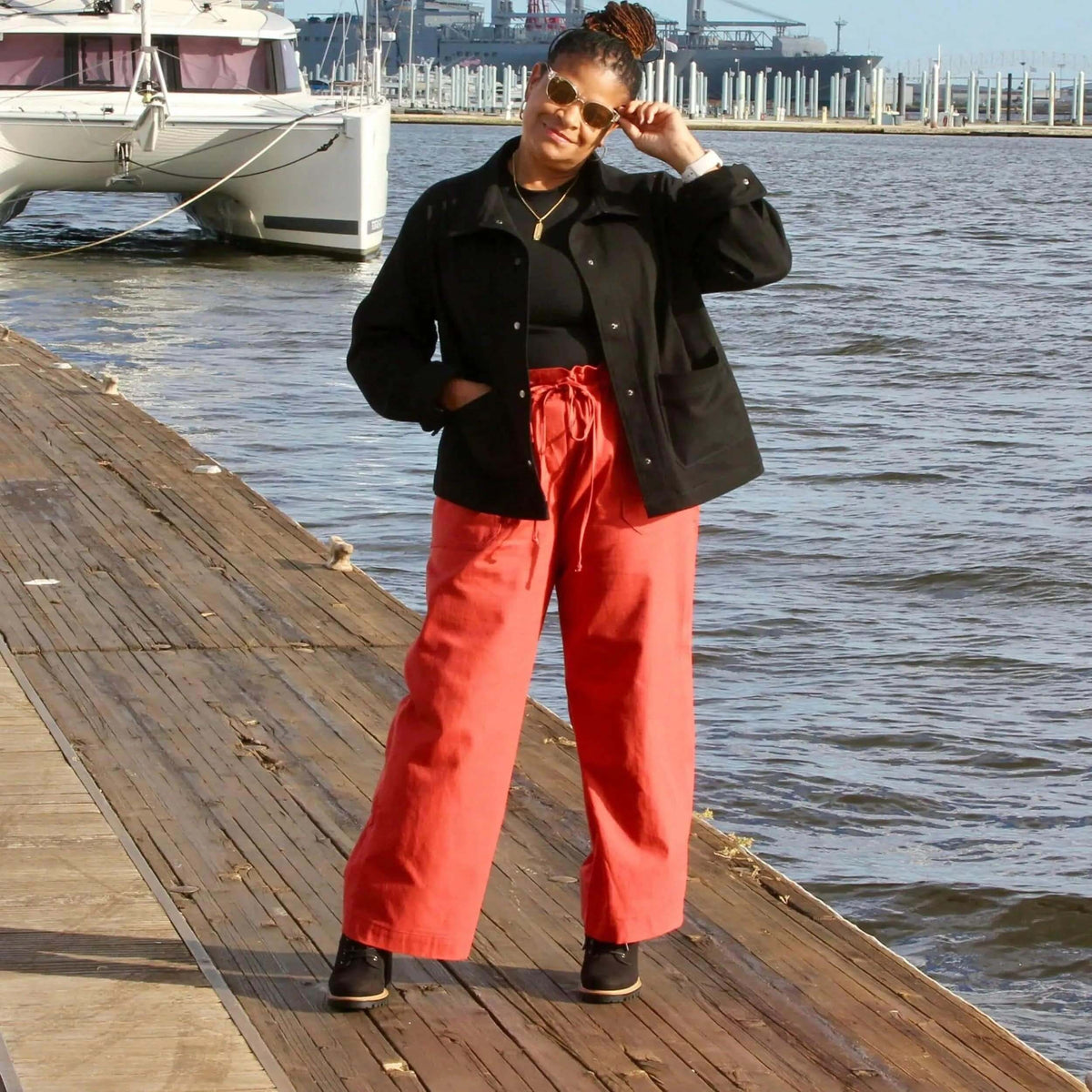 Model wearing a Canvas Jacket Paper Pattern over a black top and wide-leg orange pants by the waterfront.