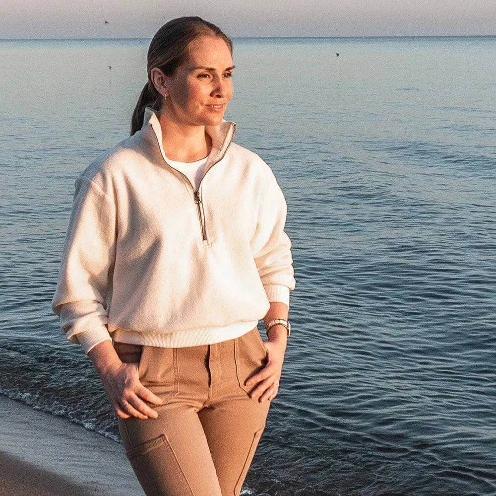 Woman wearing a Half-Zipper Sweater Paper Pattern by the beach at sunset, showcasing sporty style and comfort.