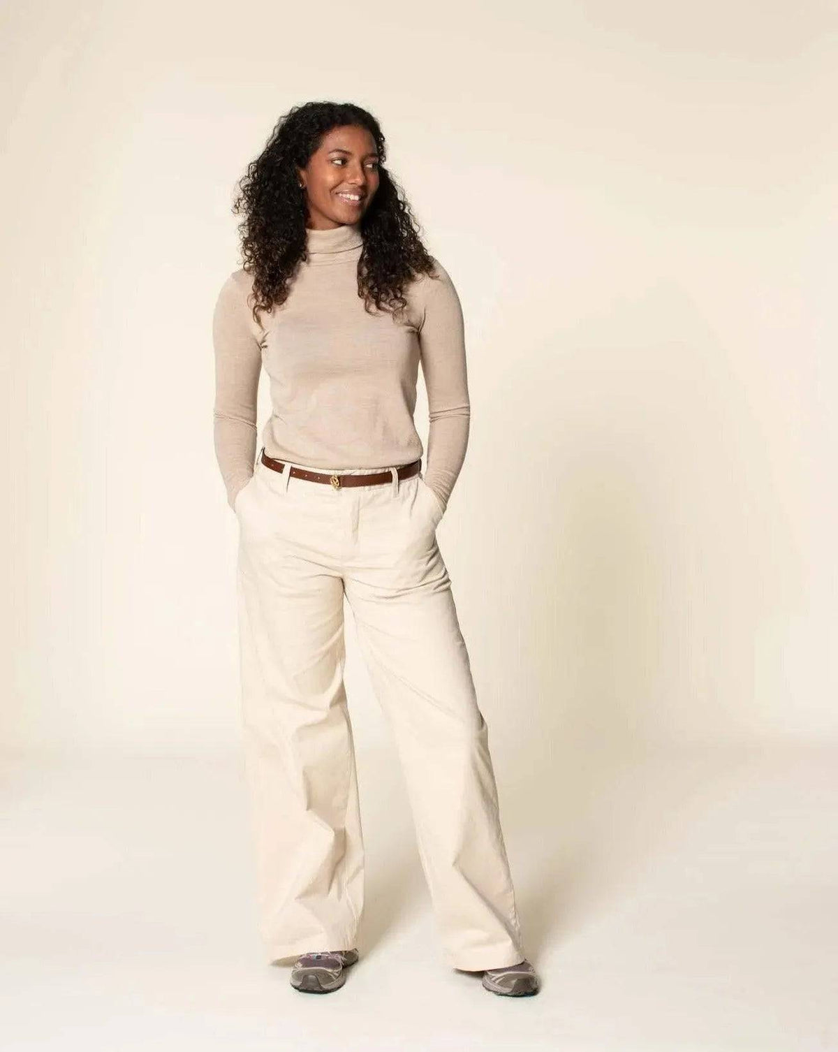 Woman wearing fitted Hepburn Pants Paper Pattern with a beige turtleneck and a stylish belt.