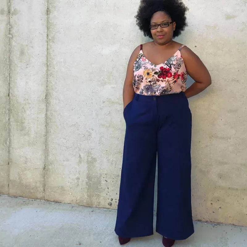 Woman wearing Hepburn Pants Paper Pattern with floral top against a concrete wall, showcasing stylish pants design.