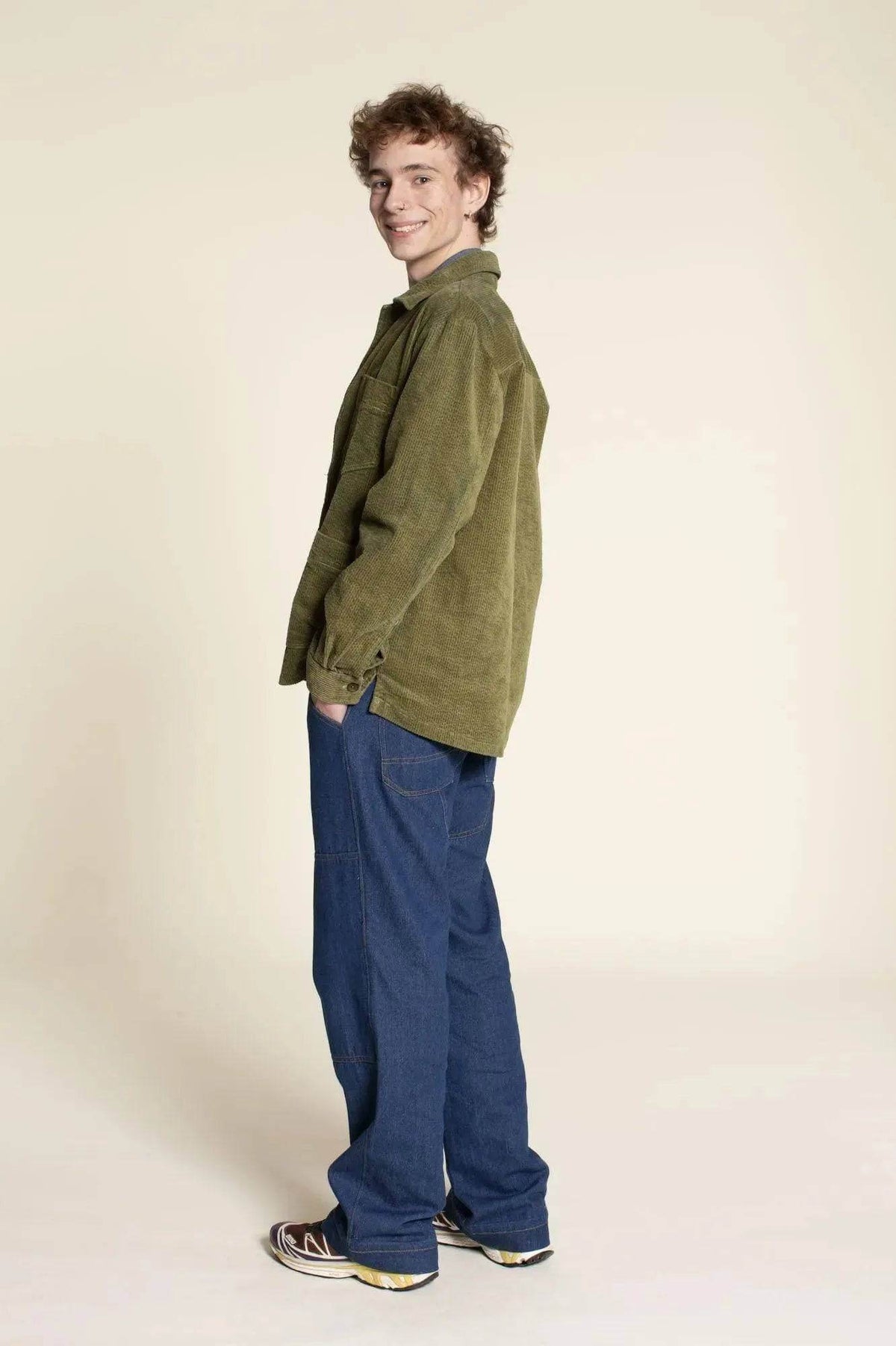 Young man wearing an Overshirt Jacket Paper Pattern in olive green, styled with casual blue pants in a side profile.