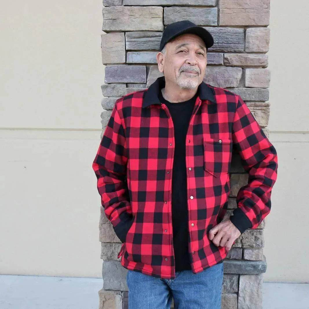 Man wearing an Overshirt Jacket Paper Pattern in red and black plaid design, standing against a stone wall.