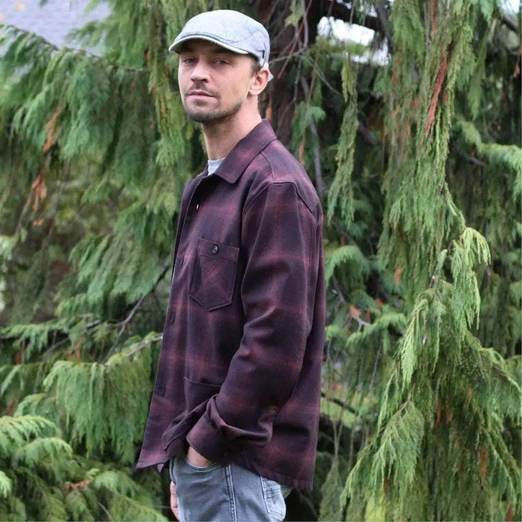 Man wearing an Overshirt Jacket Paper Pattern, standing among greenery with a stylish cap.
