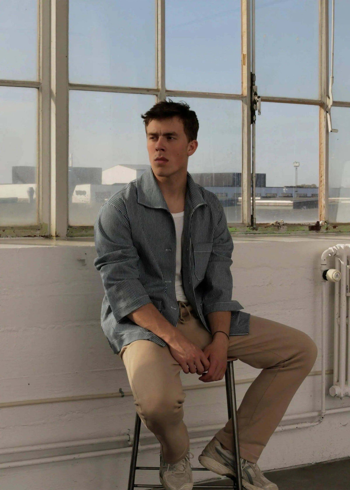 Man sitting in a chair wearing a Painter jacket Paper Pattern in a bright room with large windows.