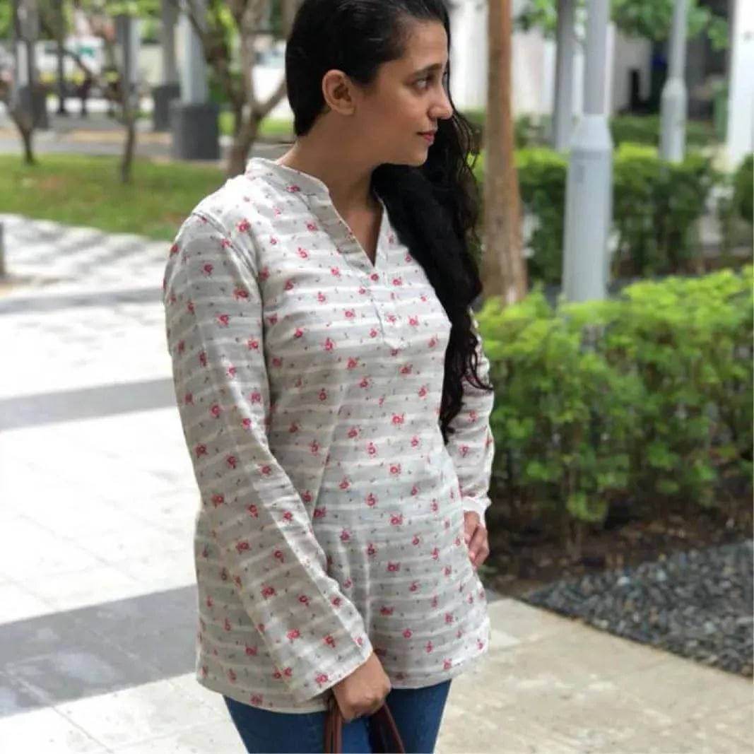 Woman wearing a stylish Perfect Tunic Paper Pattern top with floral design, outdoors in a lush green setting.
