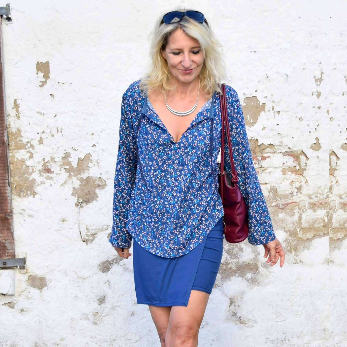 A woman wearing the Piper Tunic Paper Pattern with floral design and a blue skirt, showcasing its trendy style.