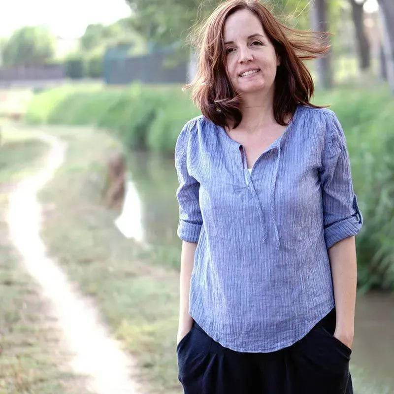 Woman wearing a stylish blue Piper Tunic Paper Pattern standing by a scenic pathway.