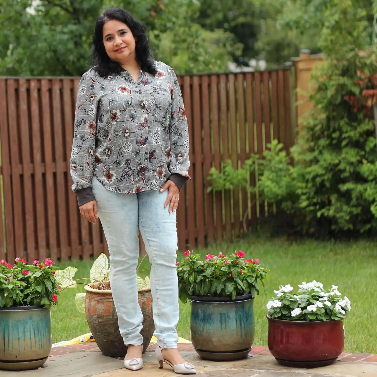 Woman wearing the Savannah shirt Paper Pattern in a garden, styled with blue jeans and elegant shoes.