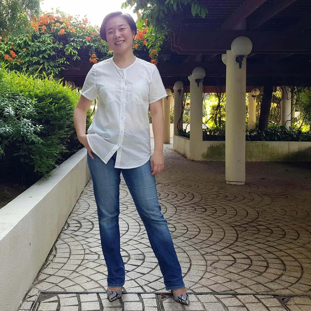 Woman wearing a stylish white Savannah shirt Paper Pattern with blue jeans in a garden setting.