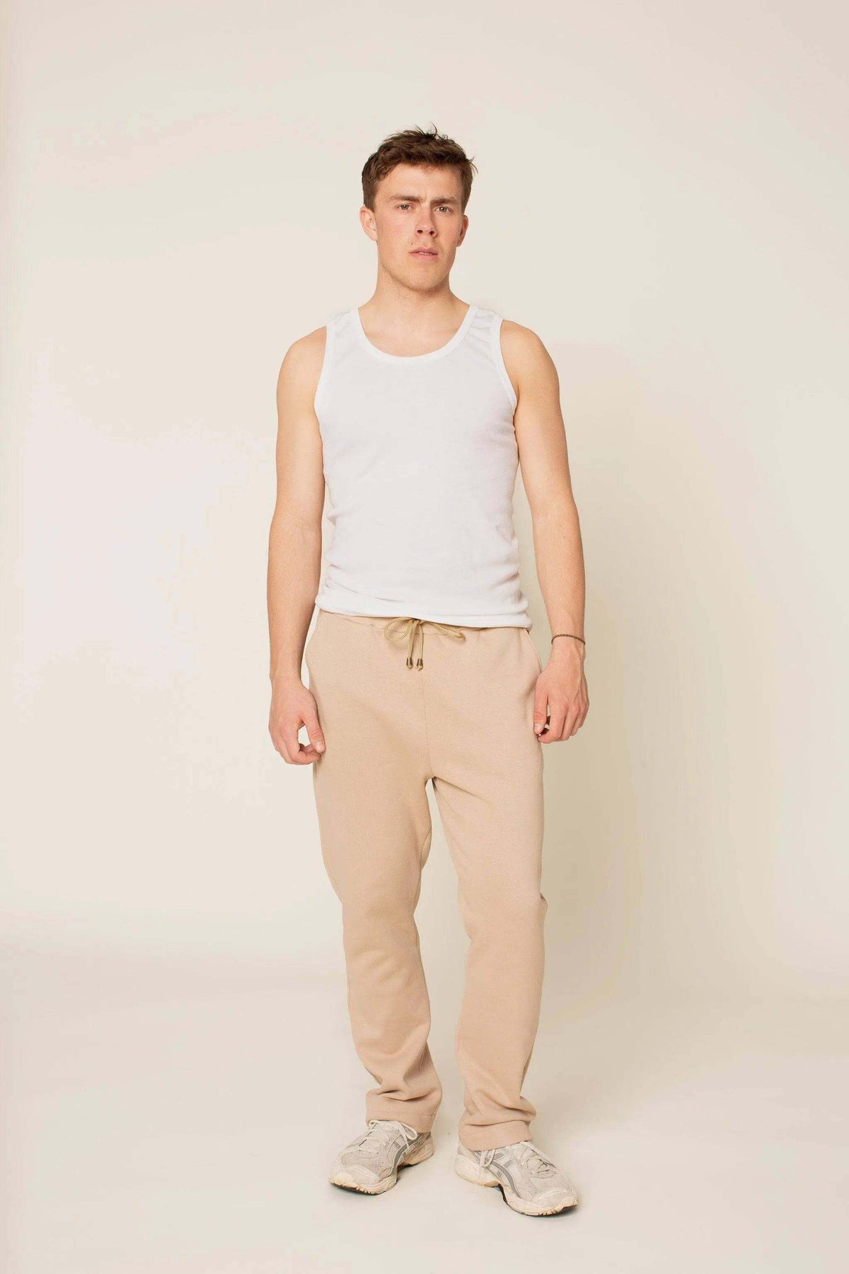 Young man wearing Rebel Sweatpants Paper pattern in beige and a white tank top, showcasing a relaxed style.
