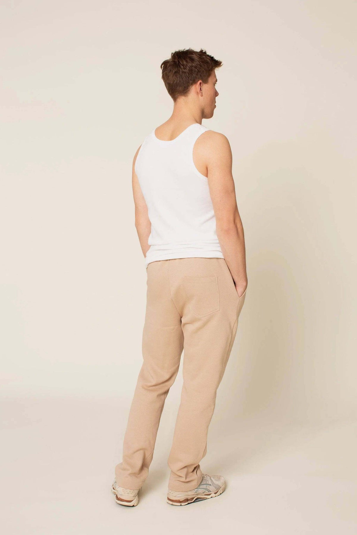 Back view of a man wearing the Rebel Sweatpants Paper pattern with a white tank top and beige sweatpants.