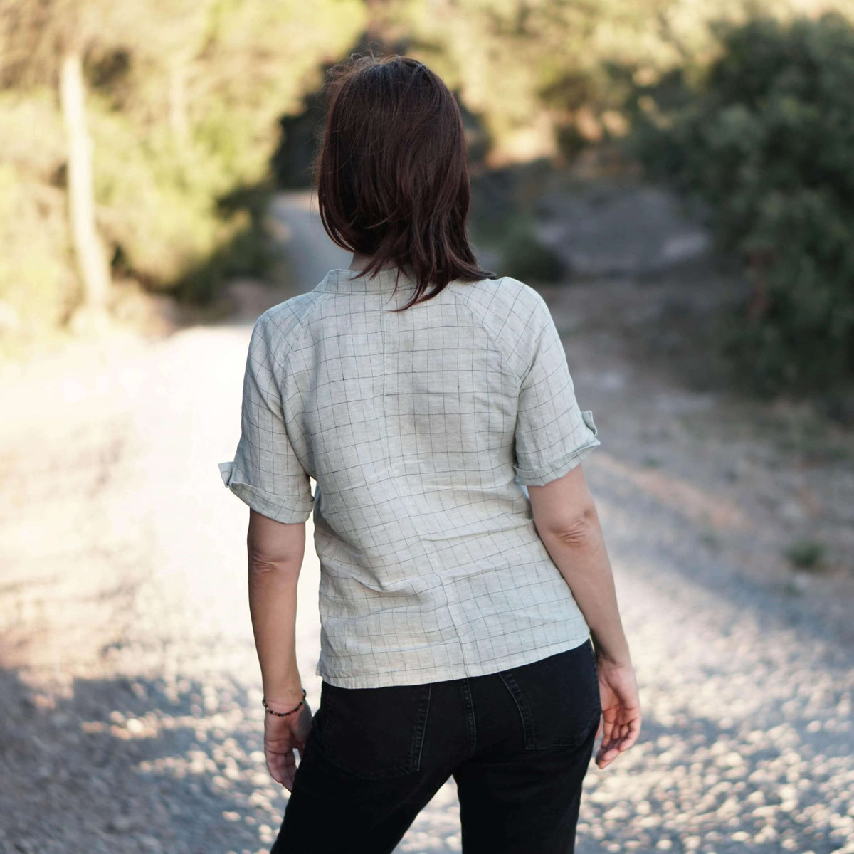 Woman wearing a casual Tropicana shirt Paper Pattern with 3/4-length sleeves, seen from the back on a gravel path.