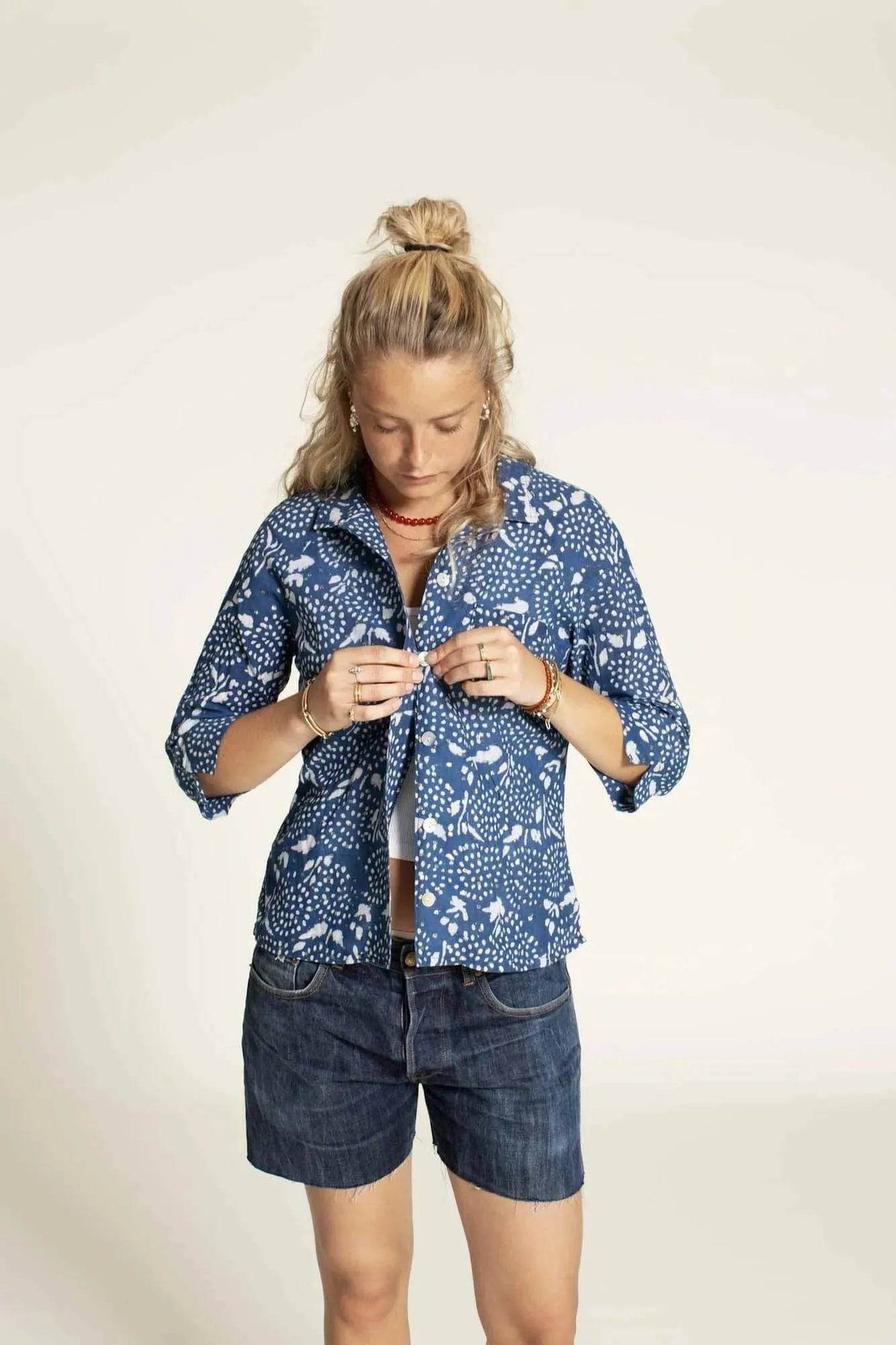 Woman buttoning the Tropicana Shirt Paper Pattern with 3/4-length sleeves and relaxed fit.