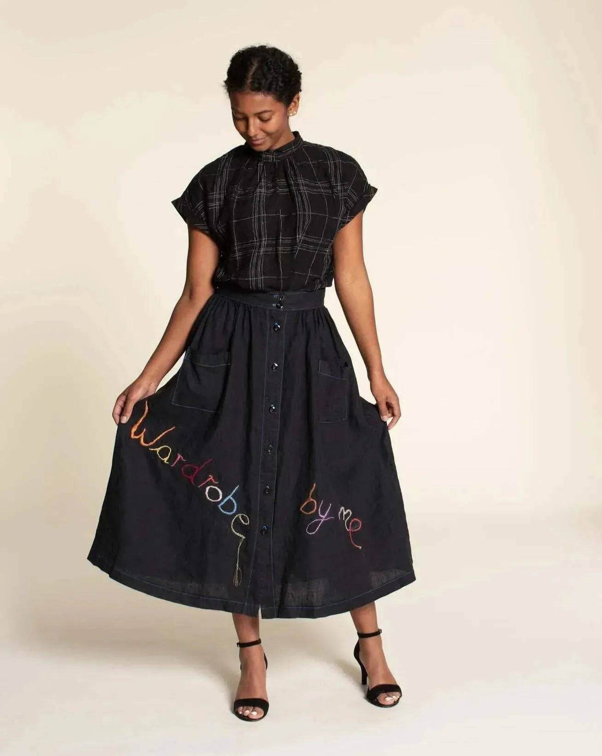Model wearing a black plaid Tulip Top Paper Pattern with a long button-up skirt featuring colorful embroidery.