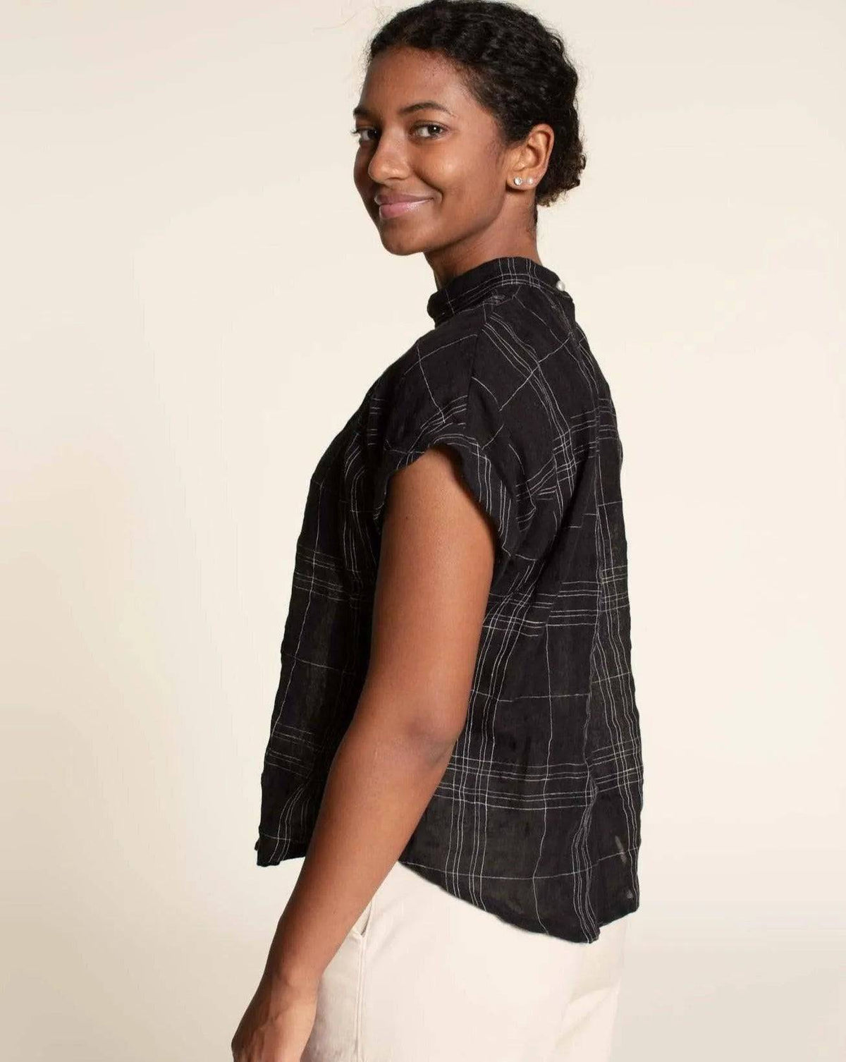Profile view of a model wearing the Tulip Top Paper Pattern in black woven fabric with rolled sleeves.