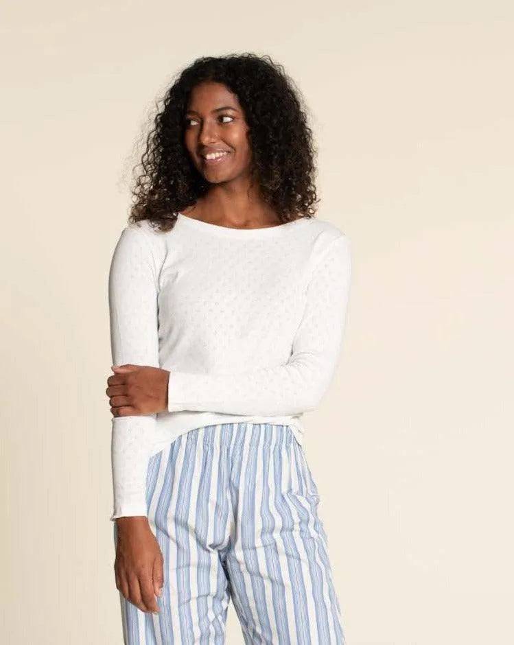 Woman wearing a fitted white T-shirt Paper Pattern with long sleeves and striped pants, smiling softly.
